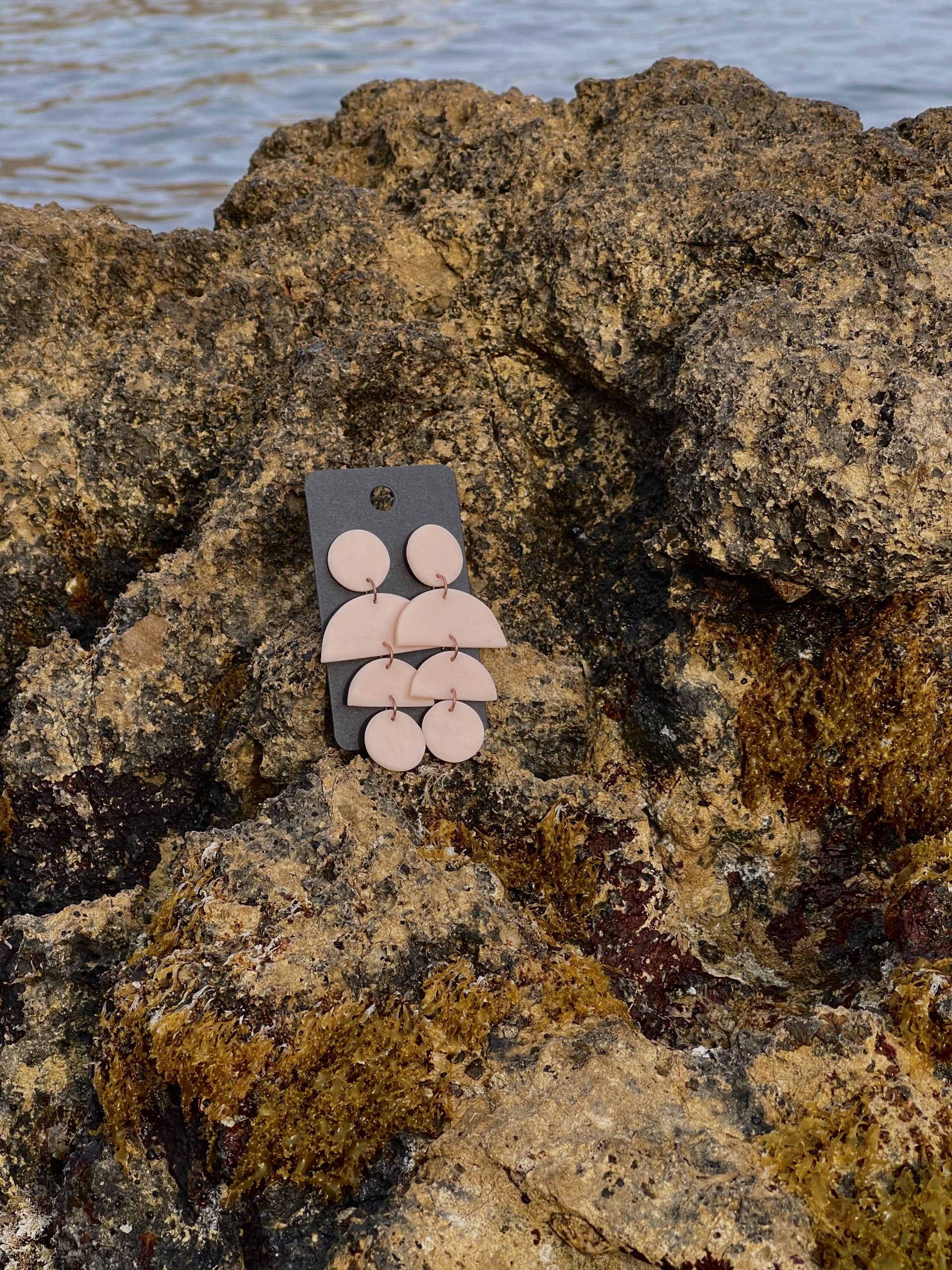close up - details - photo de près de boucles d'oreilles pendantes rose clair fait main sur un rocher en bord de mer