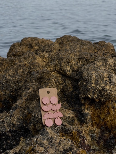 close up - details - photo de près de boucles d'oreilles pendantes longues rose brillantes fait main sur un rocher en bord de mer