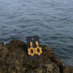 close up - details - photo de près de boucles d'oreilles pendantes mi-longues jaune moutarde fait main sur un rocher en bord de mer