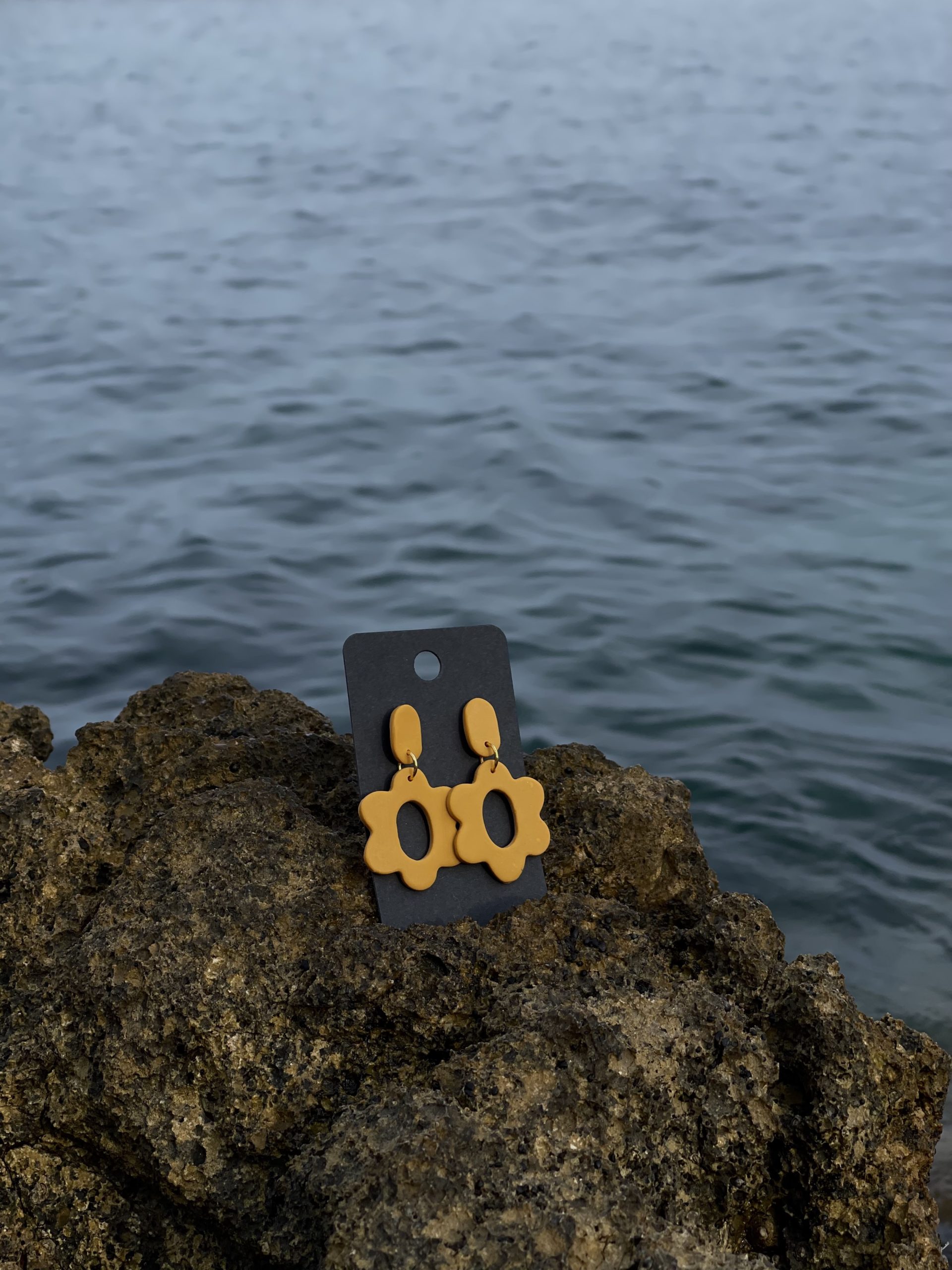 close up - details - photo de près de boucles d'oreilles pendantes mi-longues jaune moutarde fait main sur un rocher en bord de mer
