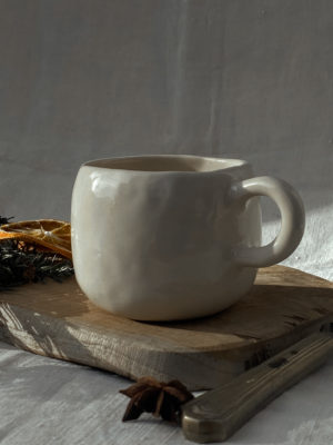 tasse crème posée sur un rondin de bois avec des oranges séchées ety des branches de sapins en fond. fond blanc cassé